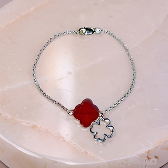 Silver bracelet with a red clover-shaped charm on a light marble background