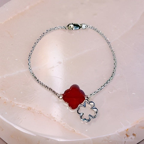 Silver bracelet with a red clover-shaped charm on a light marble background