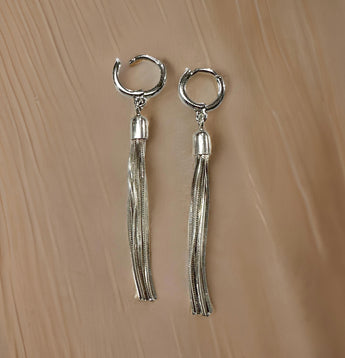 A pair of sterling silver tassel chain hoop earrings with long silver tassels, displayed against a beige background.