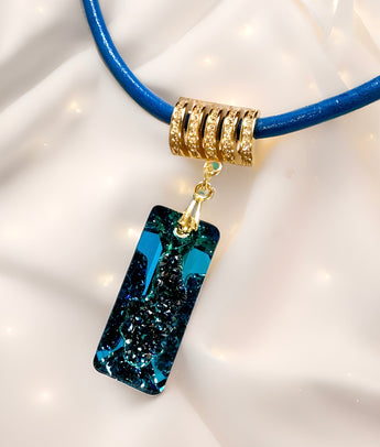 A Swarovski Bermuda blue rectangular growing crystal pendant with a gold-plated sterling silver bail, attached to a blue leather band.