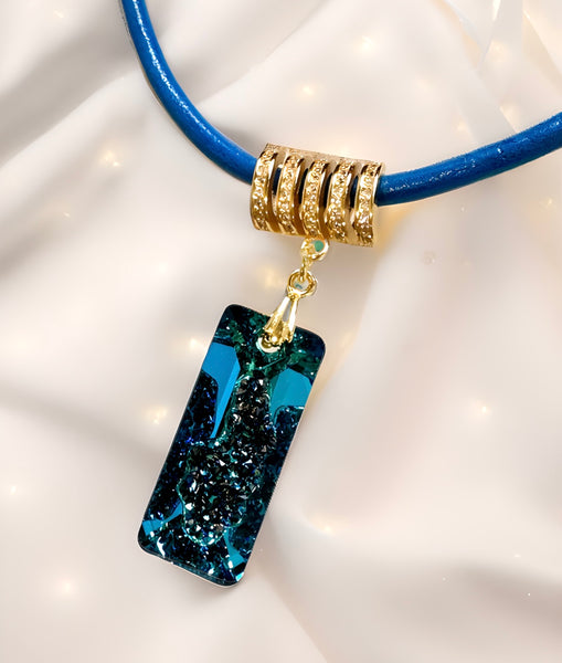 A Swarovski Bermuda blue rectangular growing crystal pendant with a gold-plated sterling silver bail, attached to a blue leather band.