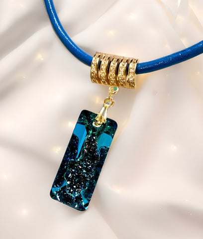 A Swarovski Bermuda blue rectangular growing crystal pendant with a gold-plated sterling silver bail, attached to a blue leather band.