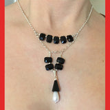 A black Swarovski crystal necklace with a drop pearl and sterling silver chains, displayed on a mannequin.
